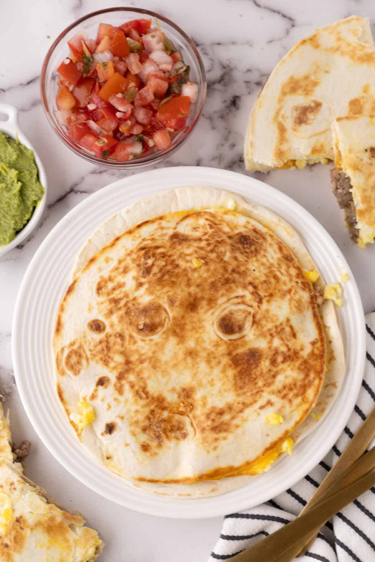 round whole golden flour breakfast quesadilla on a white plate with toppings to the side.