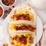 breakfast tacos with eggs cheese bacon on three flour tortillas.