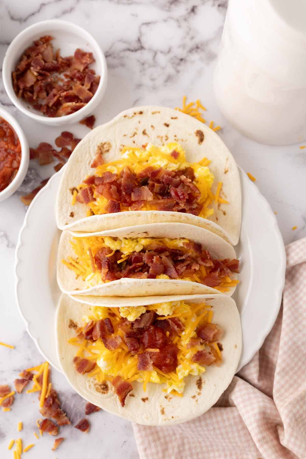 breakfast tacos with eggs cheese bacon on three flour tortillas.