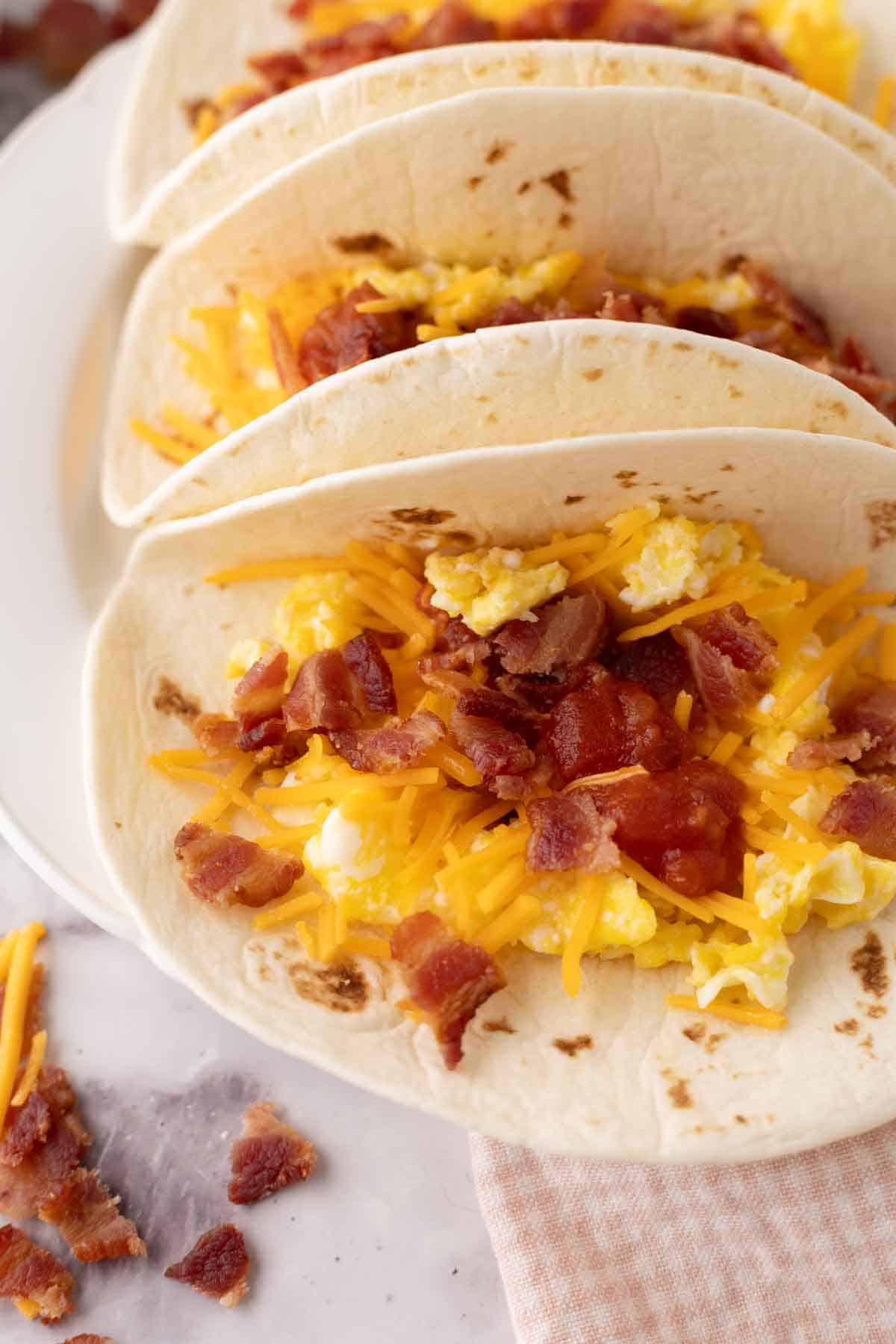 breakfast tacos with eggs cheese bacon on three flour tortillas.