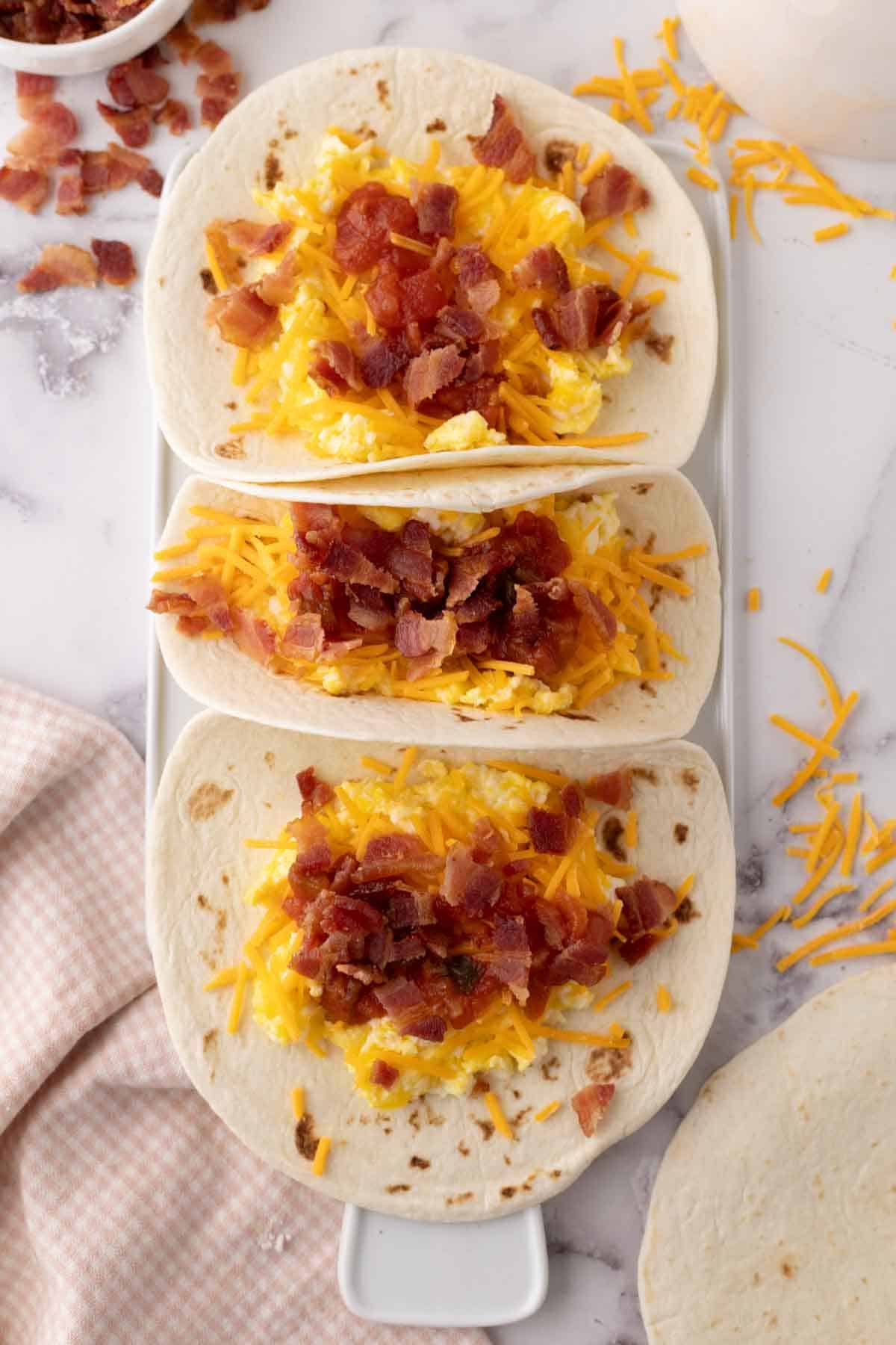 breakfast tacos with eggs cheese bacon on three flour tortillas.