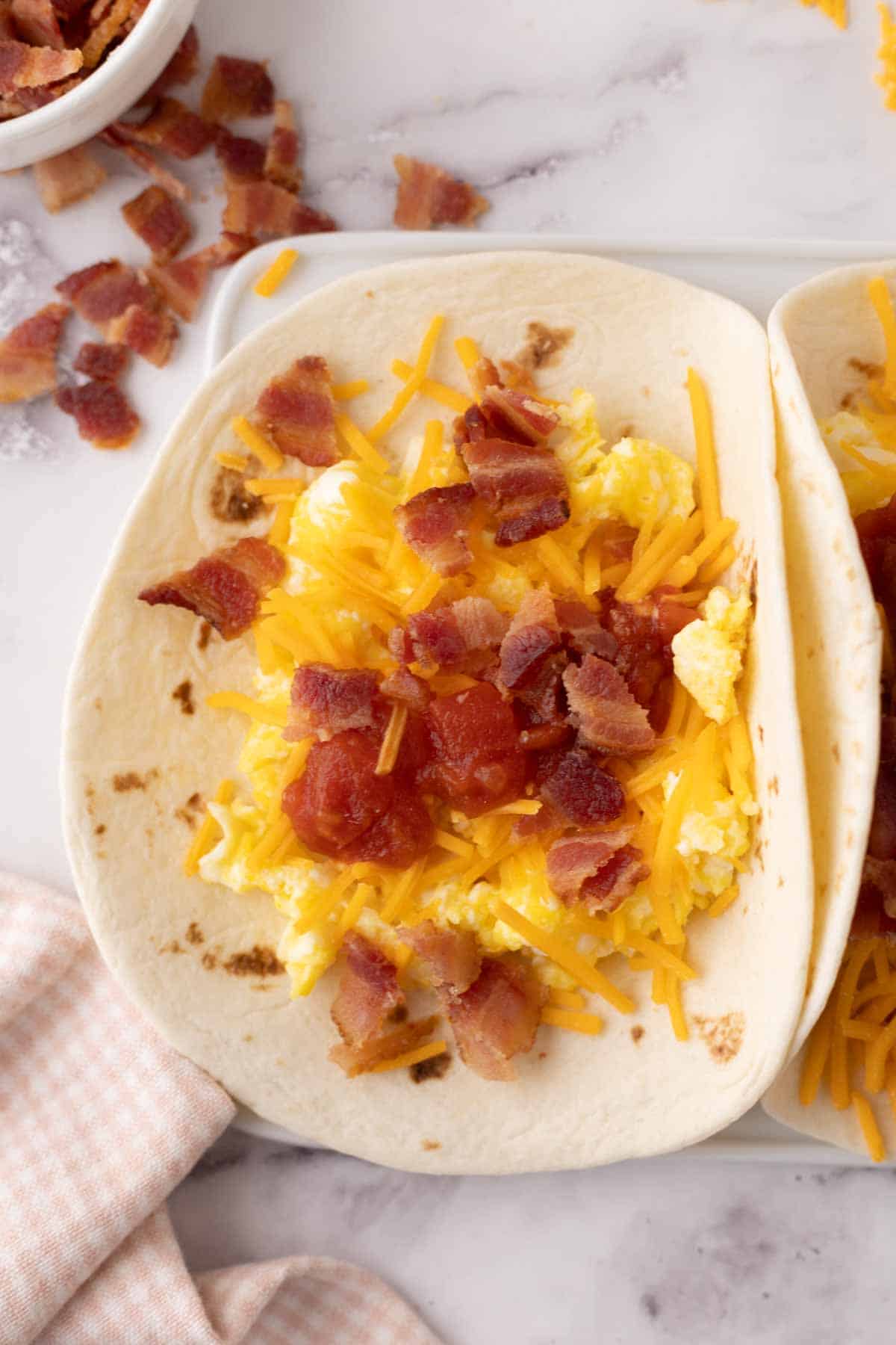 breakfast taco with eggs cheese and bacon a flour tortilla.