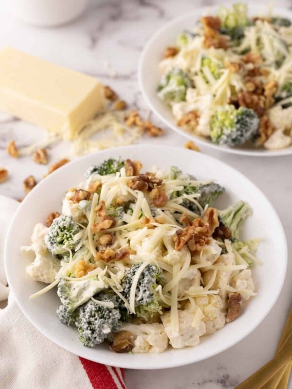 broccoli and cauliflower salad recipe with walnuts on white plates.