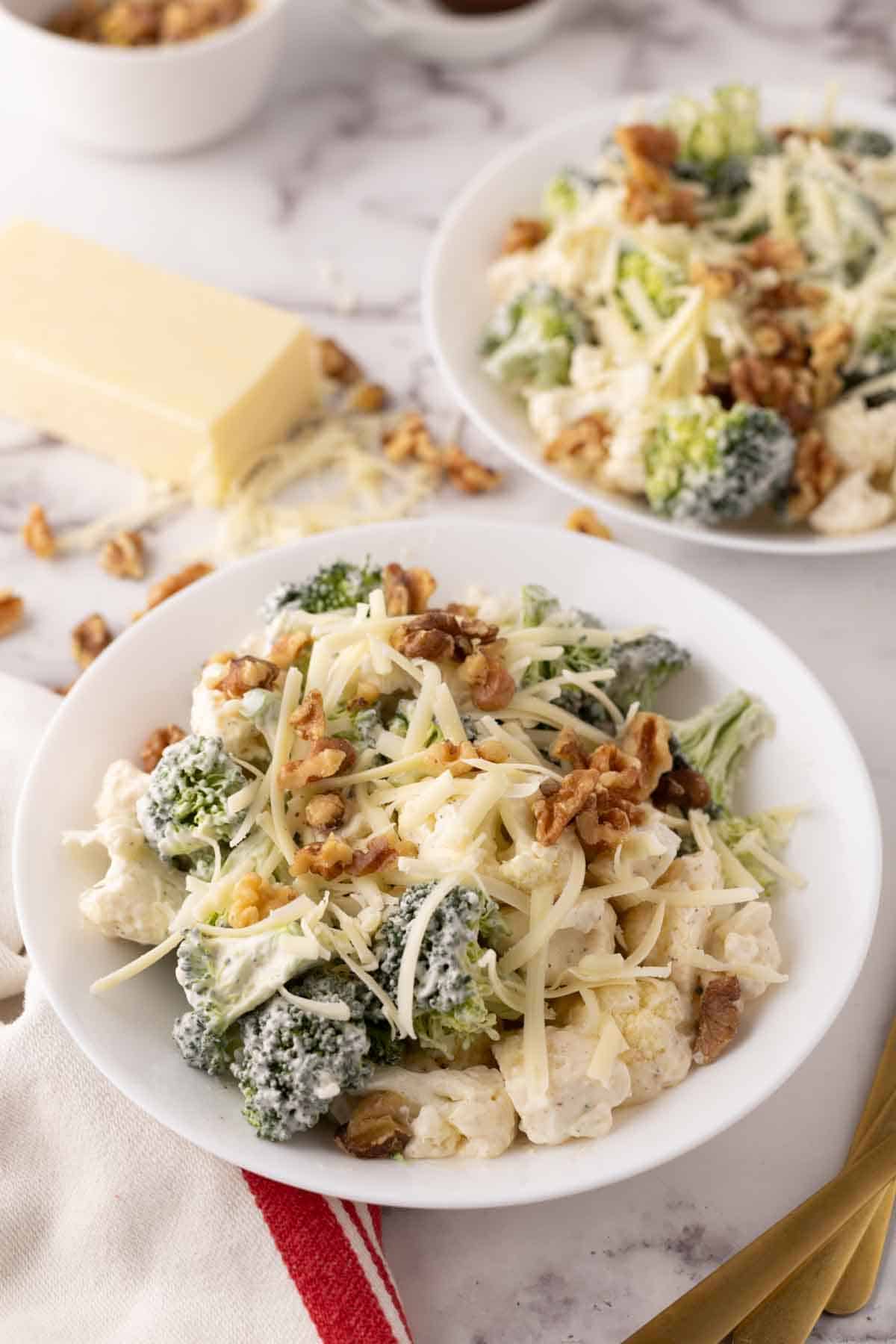 broccoli and cauliflower salad recipe with walnuts on white plates.