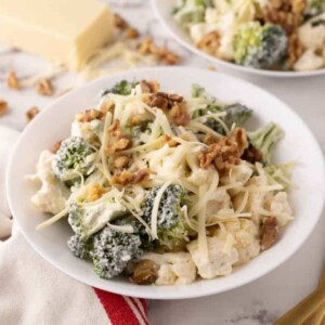 broccoli and cauliflower salad recipe with walnuts on white plates.