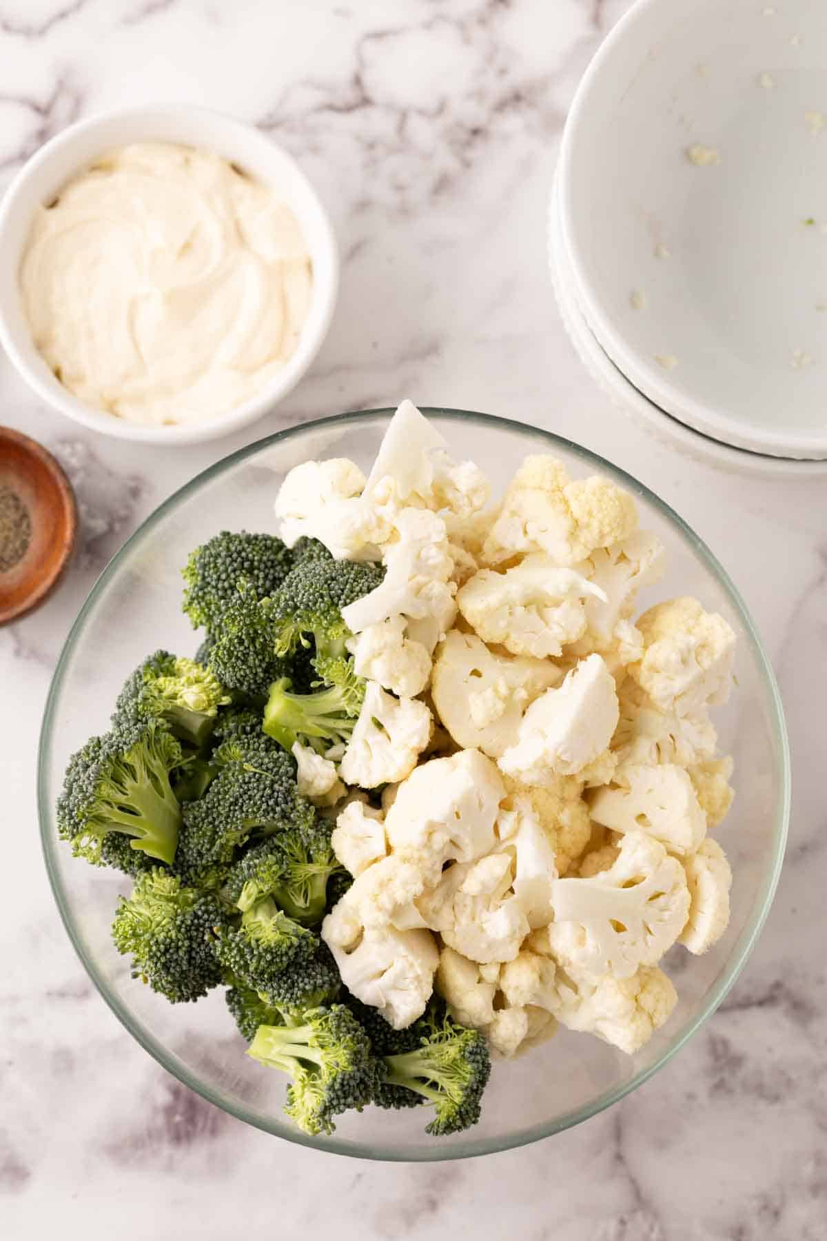 Clear mixing bowl with raw ingredient to make broccoli and cauliflower salad recipe.