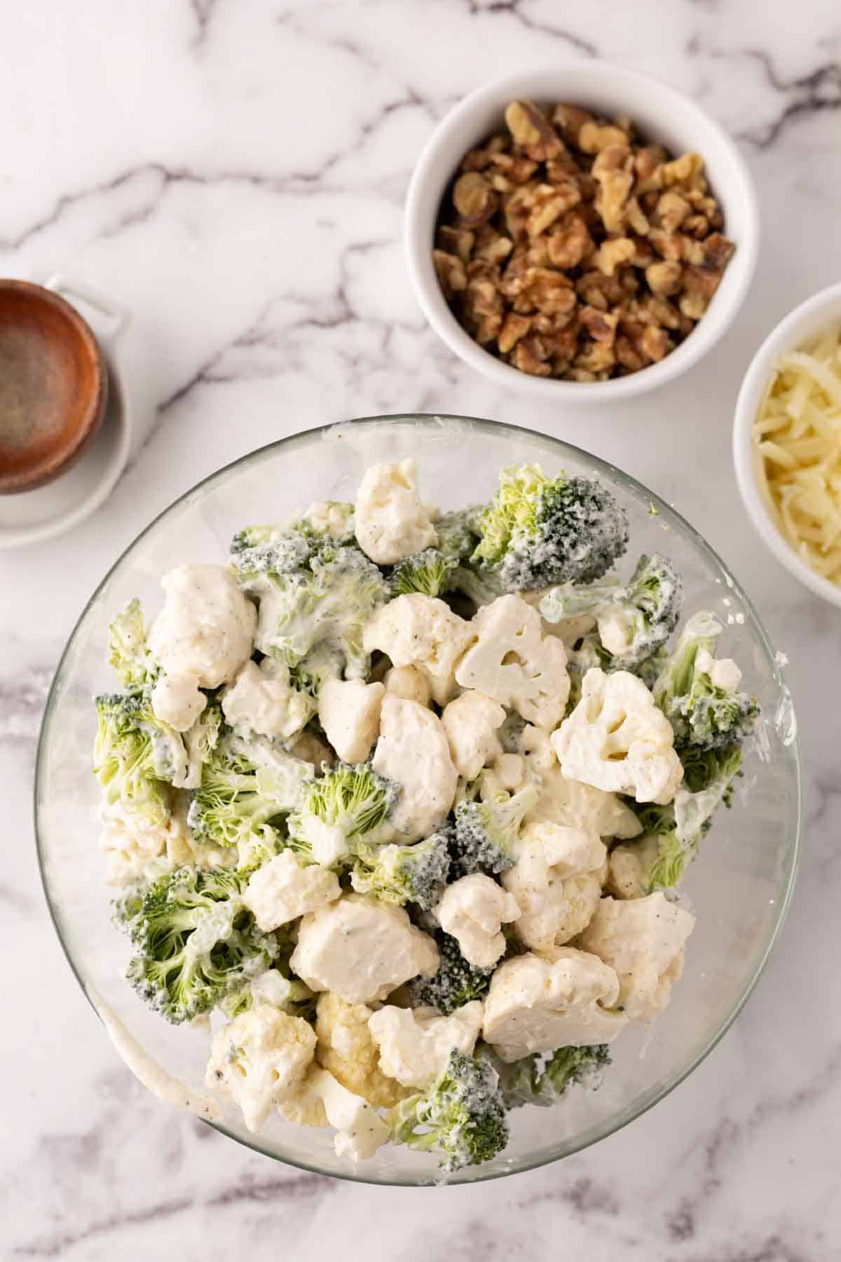 Clear mixing bowl with broccoli and cauliflower salad recipe.