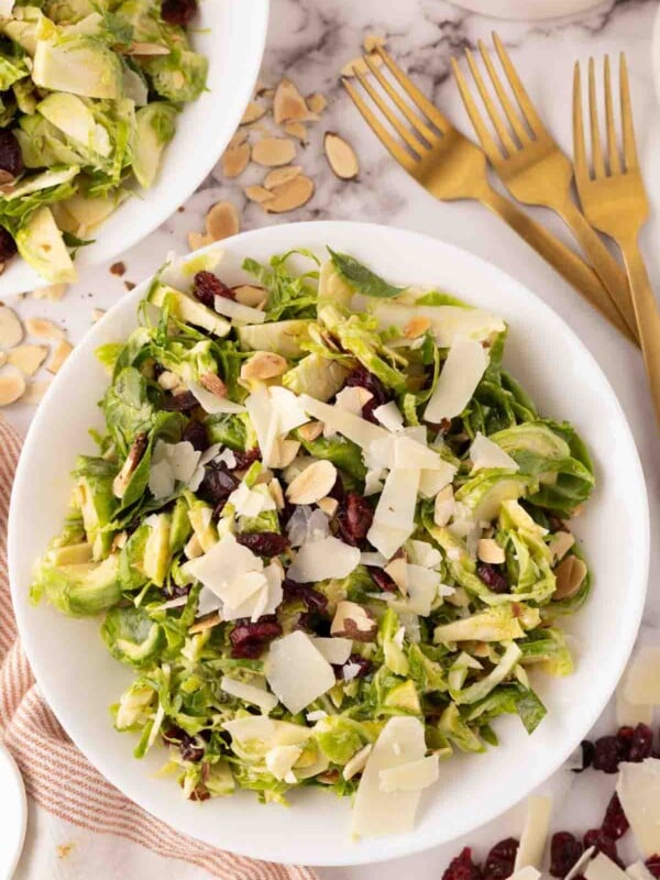 Brussels sprouts salad on a white plate with golden forks to the side.