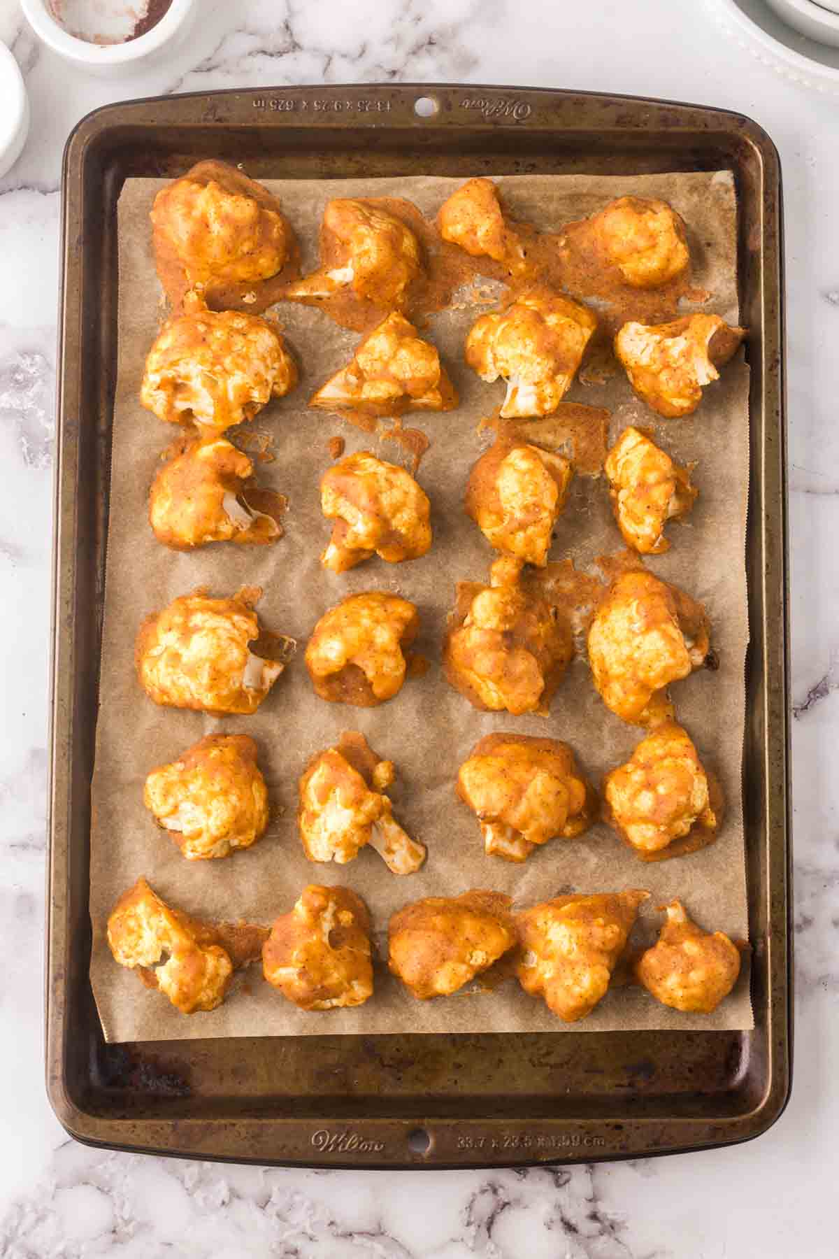 cauliflower florets with buffalo sauce on a parchment lined sheet pan.