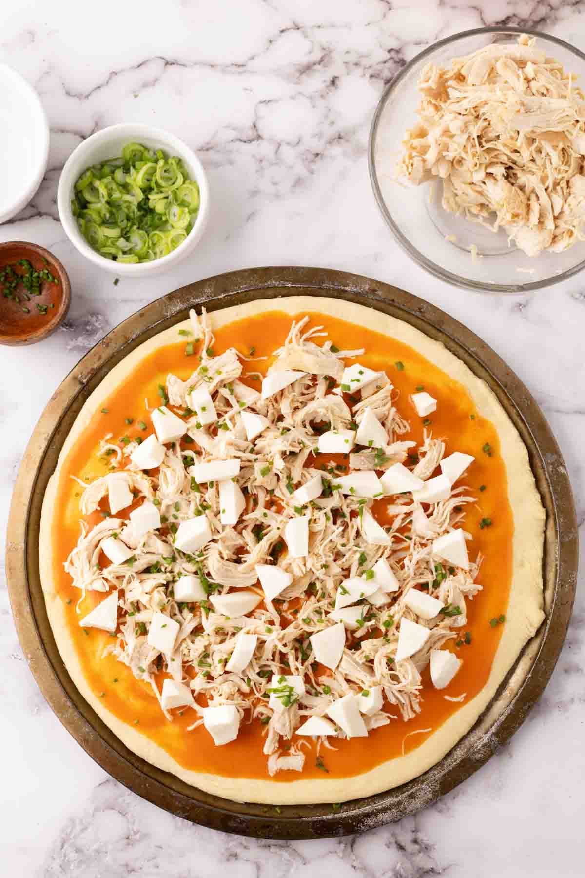 round cooking stone with raw pizza dough topped with ingredients to make buffalo pizza.