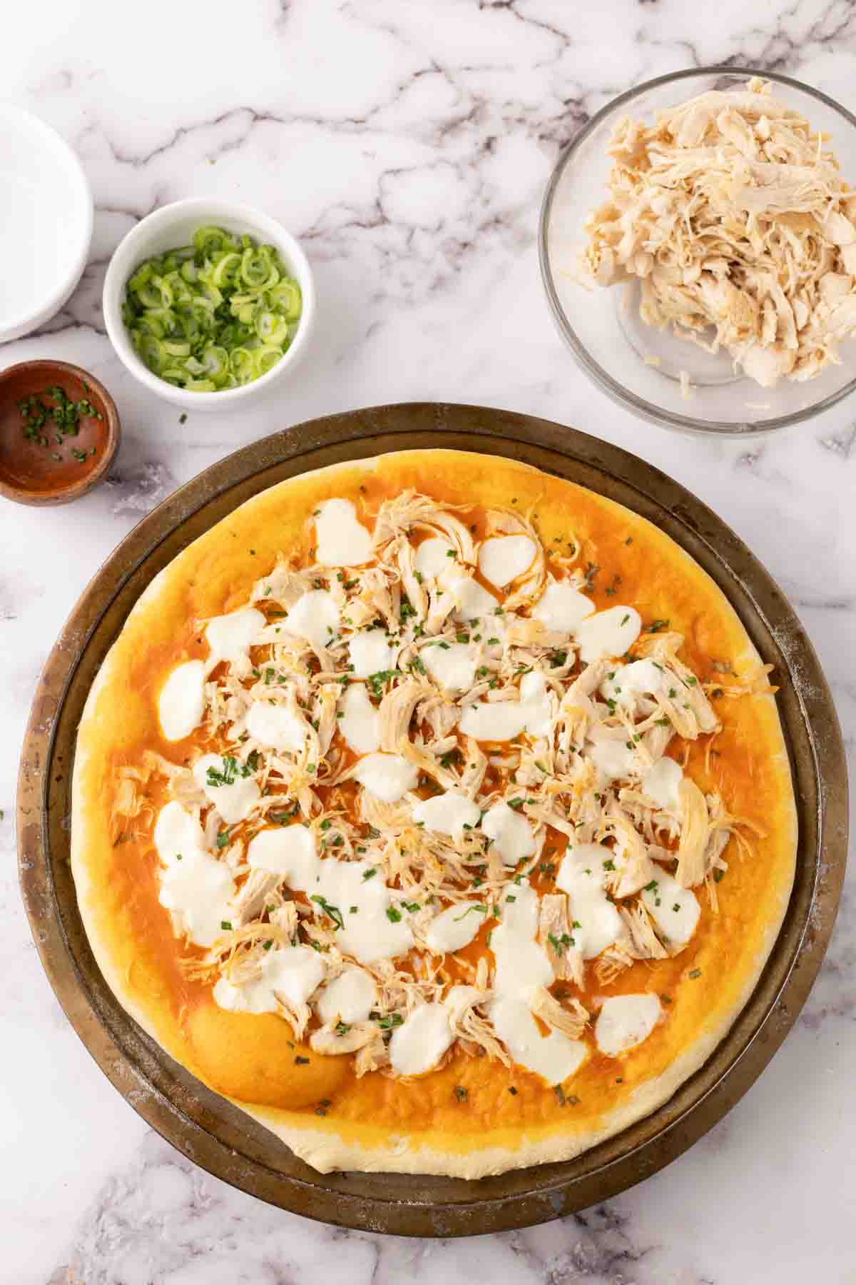 round cooking stone with raw pizza dough topped with ingredients to make buffalo pizza.