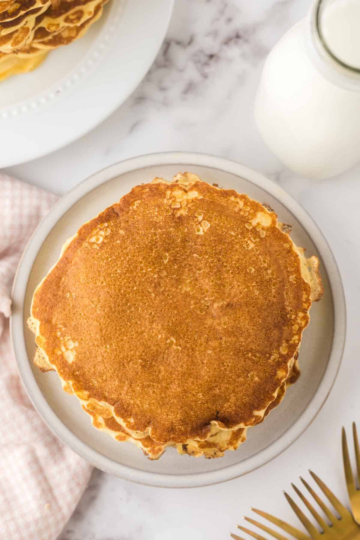 buttermilk pancakes stacked on a round plate with golden forks to the side.