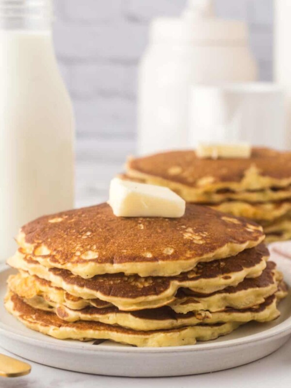 buttermilk pancakes stacked on two round plates with a pad of butter on top.