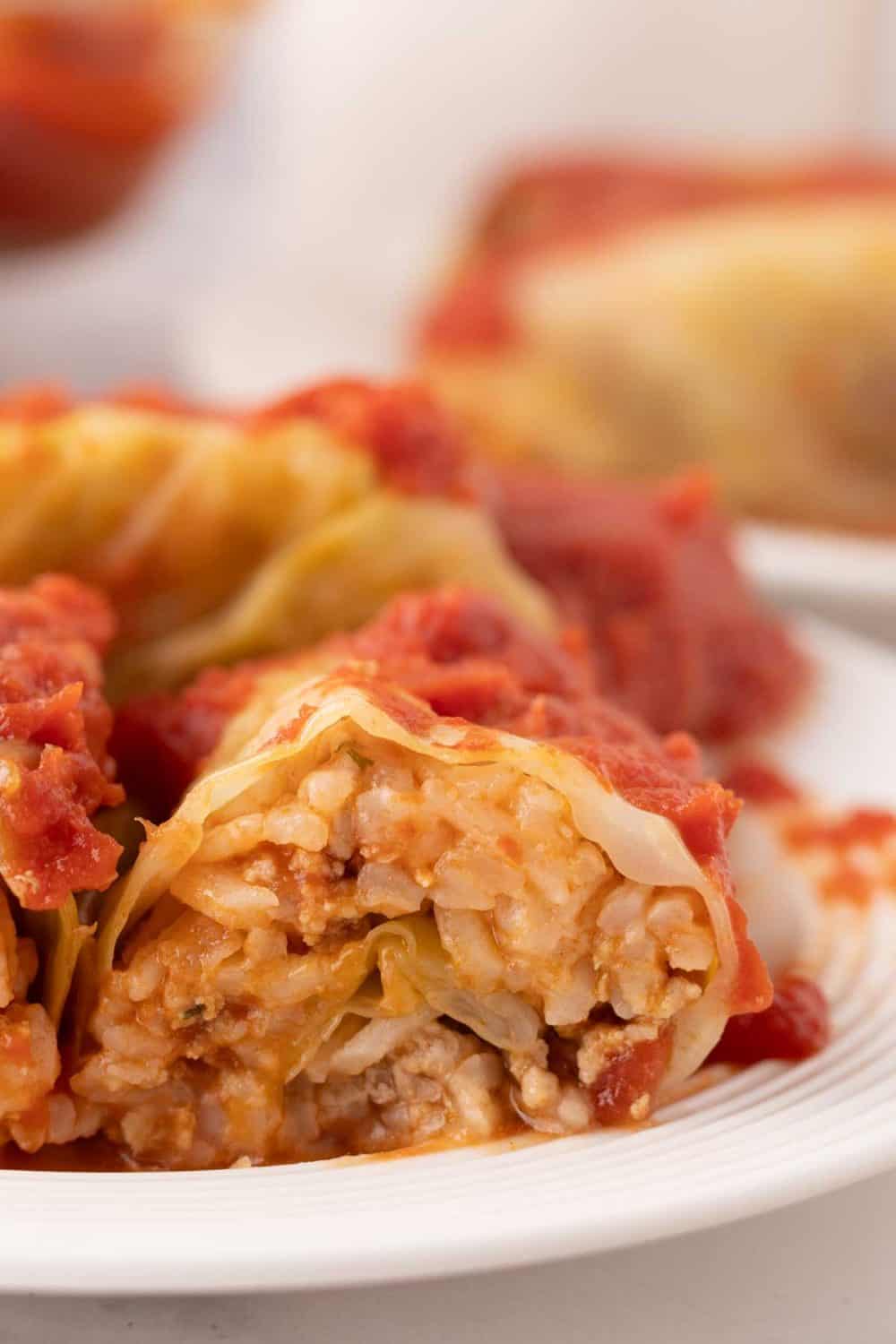 cooked cabbage rolls smothered in red sauce on a round plate sliced in half.