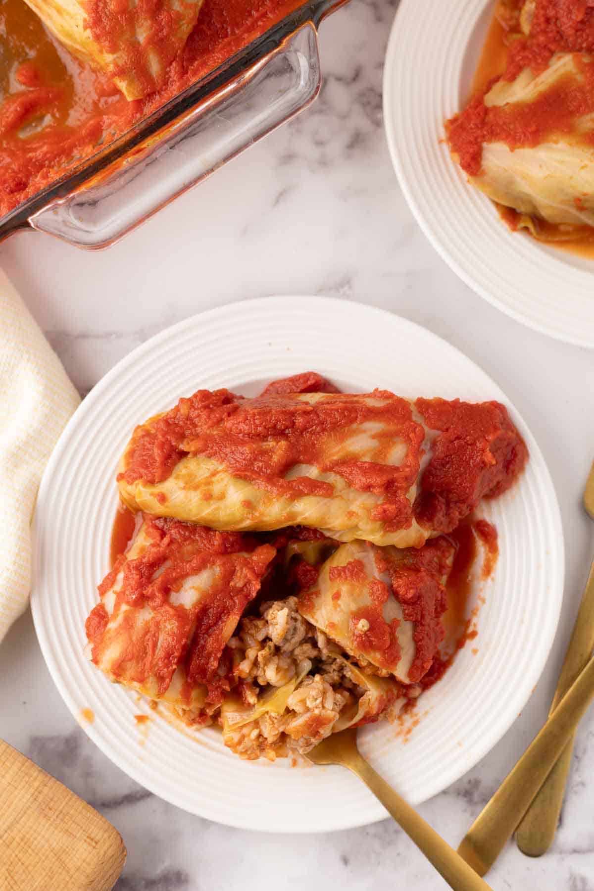 cooked cabbage rolls smothered in red sauce on a round plate with a golden fork in it.