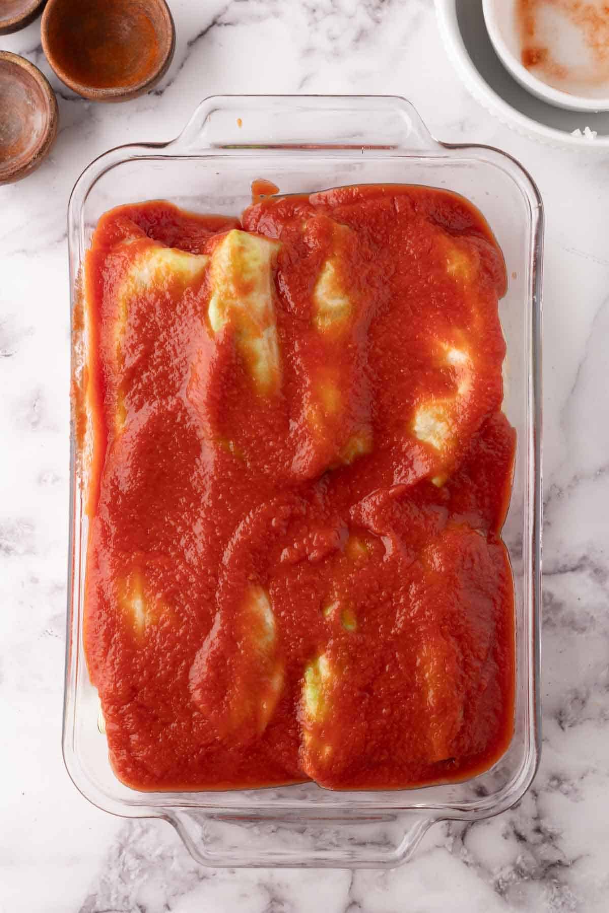 raw cabbage rolls in a glass baking dish smothered in red sauce.