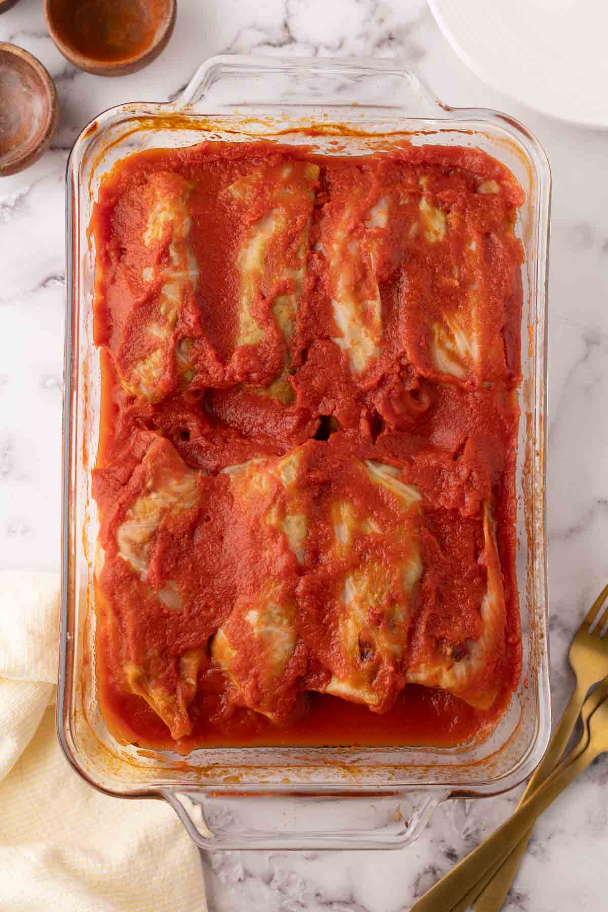 cooked cabbage rolls in a glass baking dish smothered in red sauce.