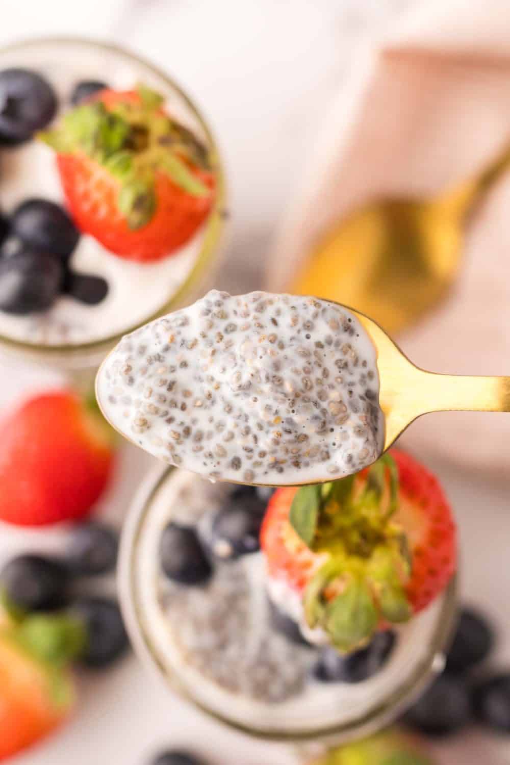 chia seed pudding spooned over small mason jars with strawberries and blueberries.