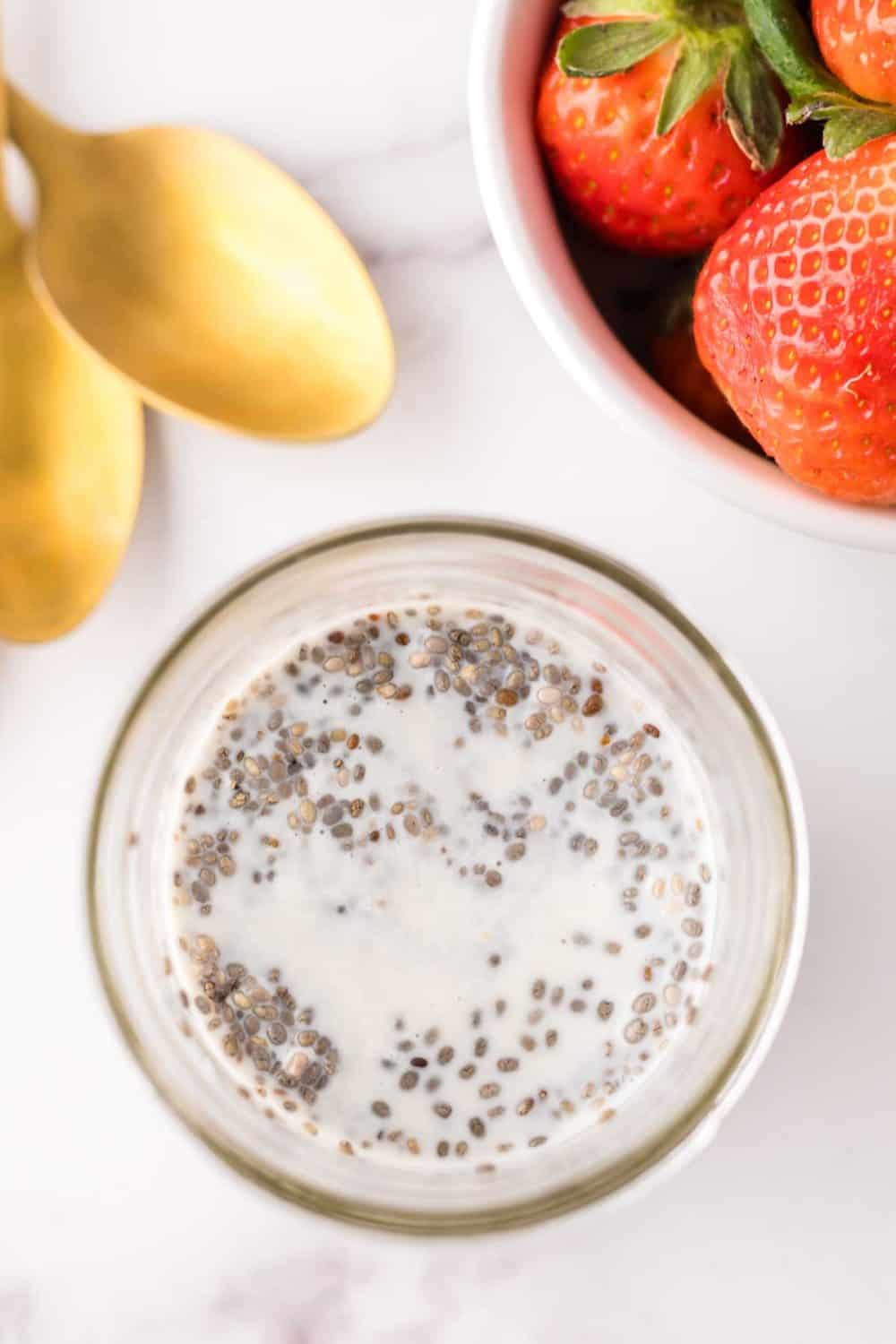 chia seed pudding in small mason jars with golden spoons and strawberries to the side.