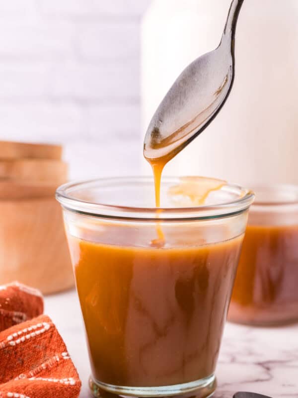 glass jar filled with homemade caramel sauce being spooned out.