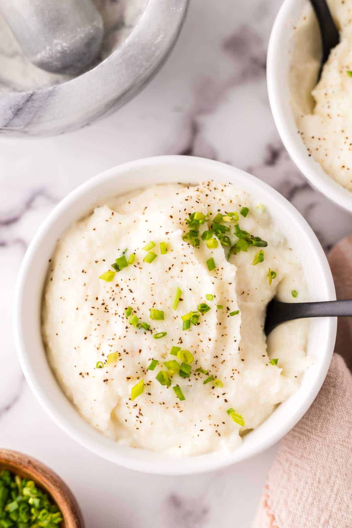 small white bowl with cauliflower mashed potatoes with seasonings on top.