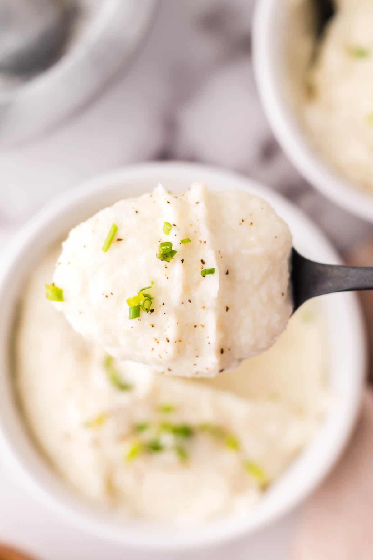 black spoonful of cauliflower mashed potatoes over a small portion bowl.