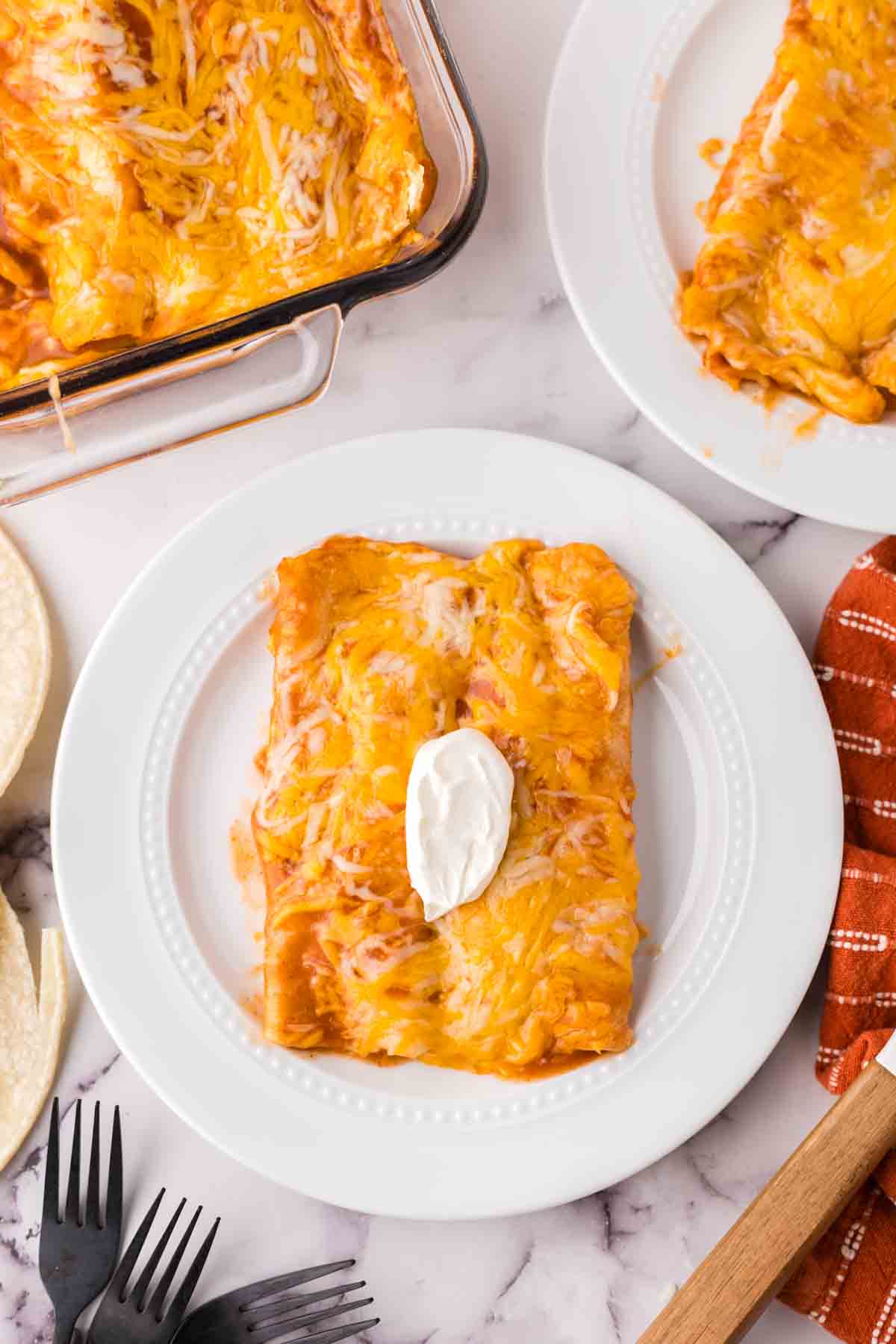 cheese enchiladas on a white plate with sour cream on top.