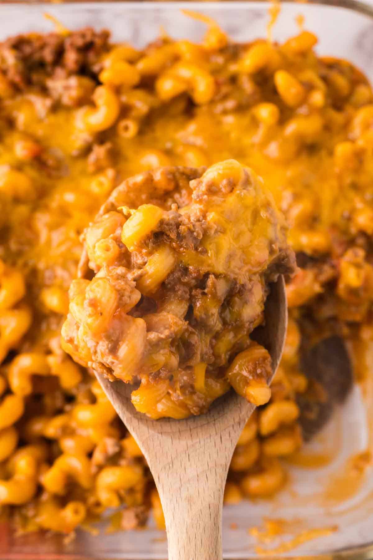 wooden spoon over a small clear baking dish with the cheeseburger casserole recipe.