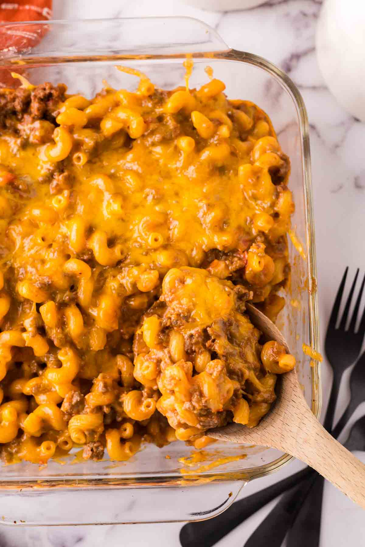 wooden spoon over a small clear baking dish with the cheeseburger casserole recipe.