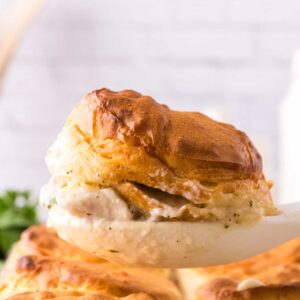 white spoon pulling a biscuit out of casserole dish with the chicken and biscuits recipe.