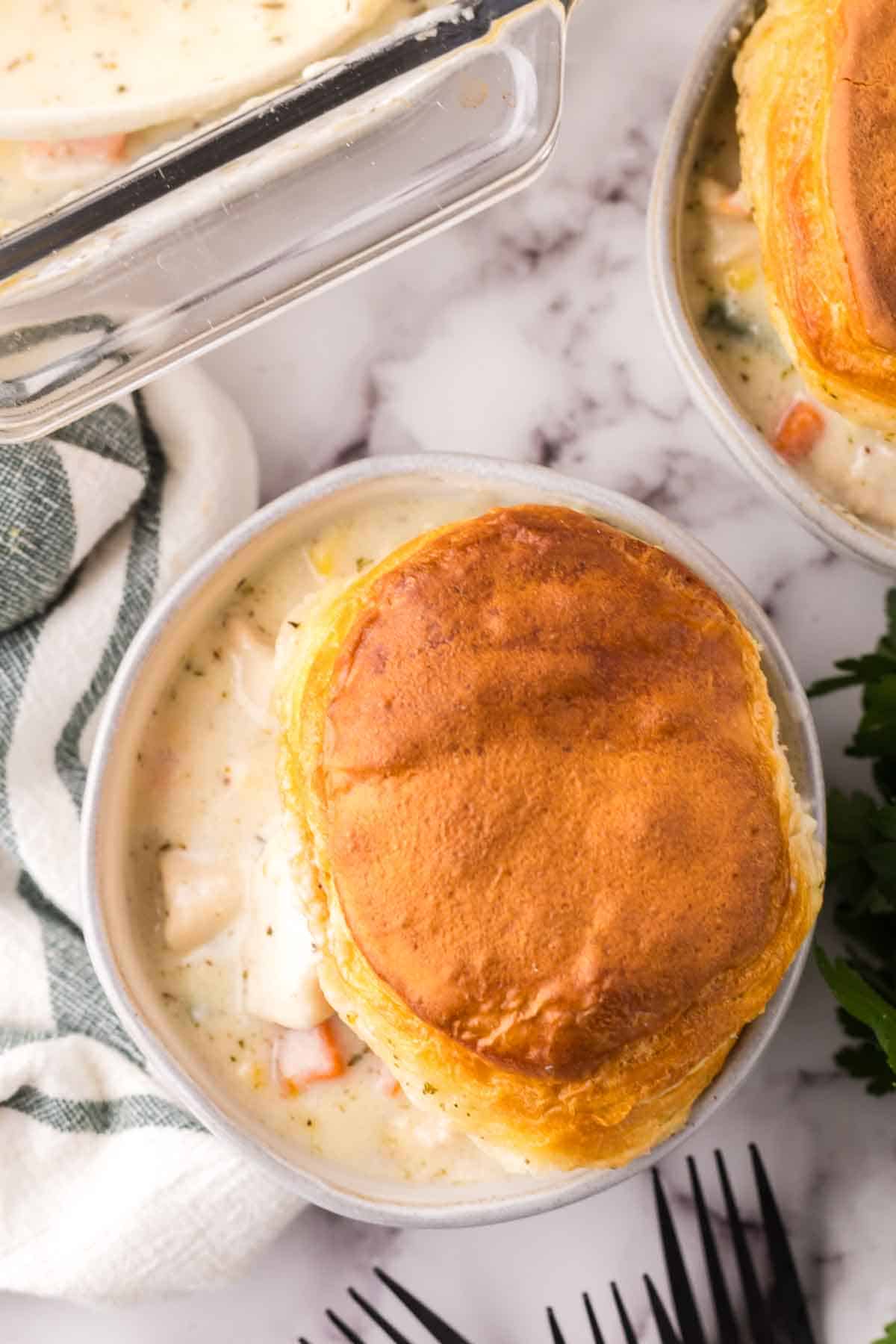 white bowl of gravy and chicken with a biscuit on top.