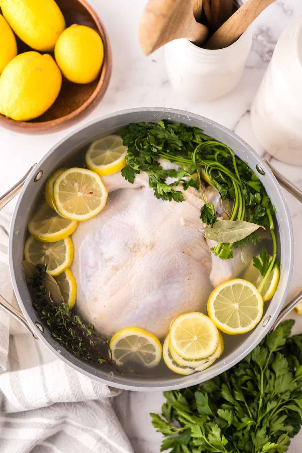 whole chicken in a large stock pot brining in sliced lemon and herbs.