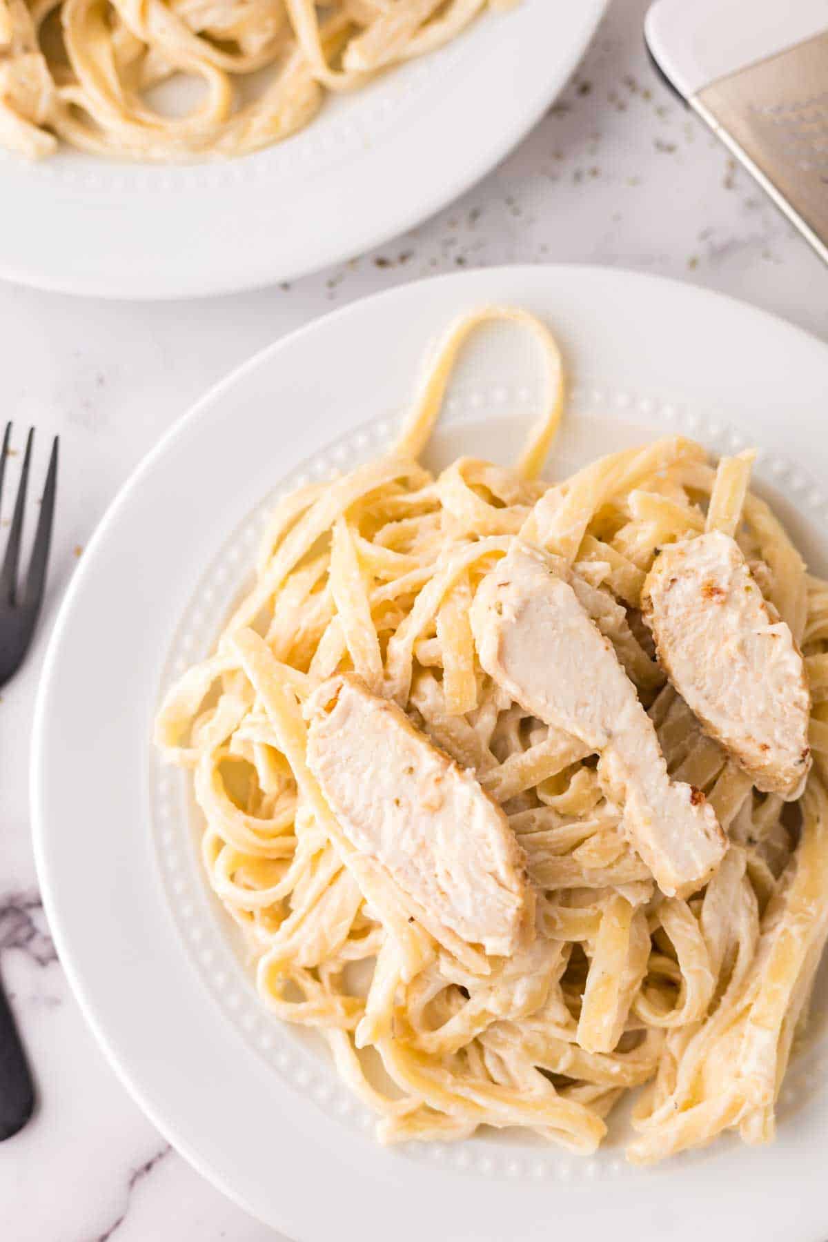 chicken fettuccine alfredo in a white serving bowl with parmesan cheese.