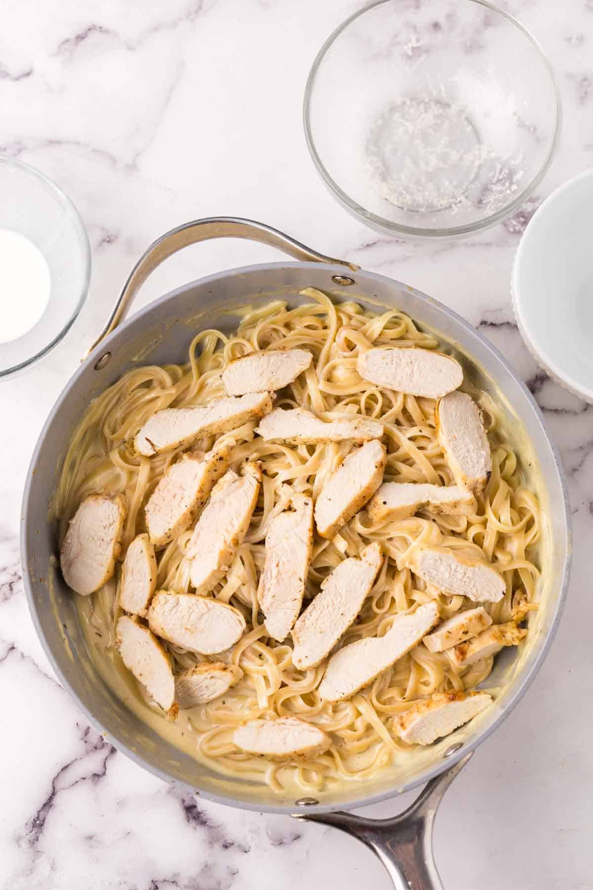 sauce pan adding chicken to finish off the chicken fettuccine alfredo recipe.