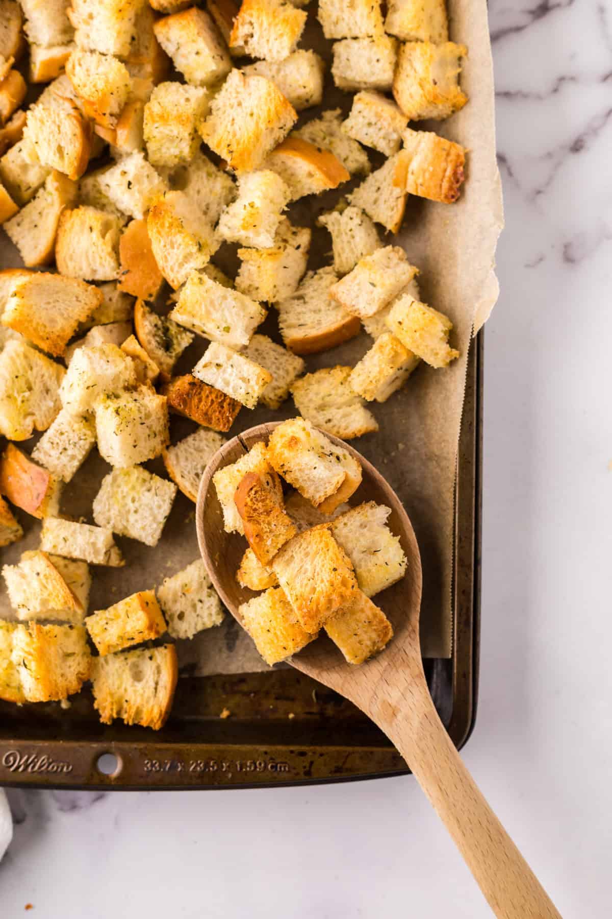 wooden spoon over a bakings sheet fresh from the oven with homemade crouton recipe.