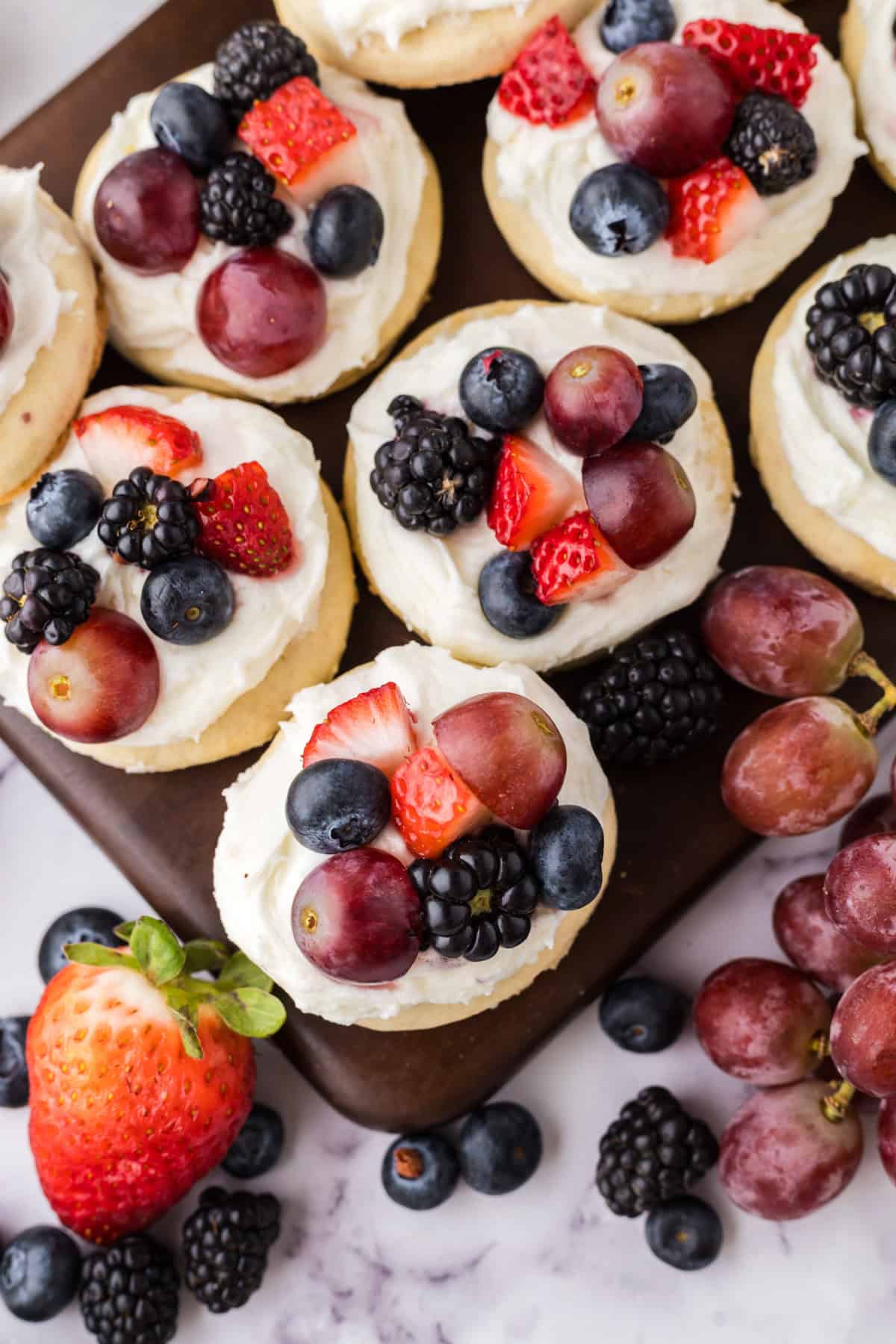 fresh fruit atop fruit pizza cookies on a wooden board.