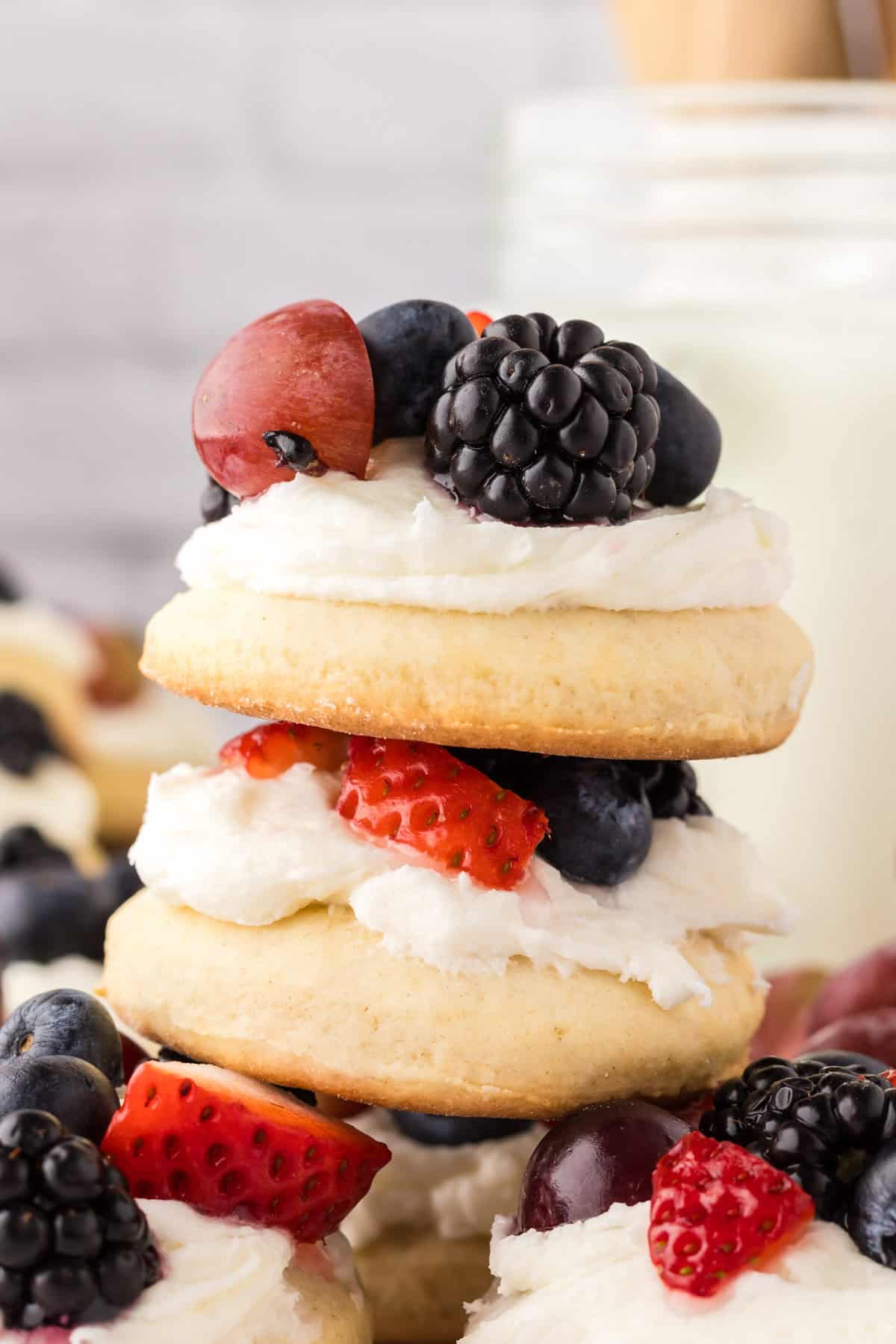 leaning stack of fruit pizza cookies with fresh fruit all around.