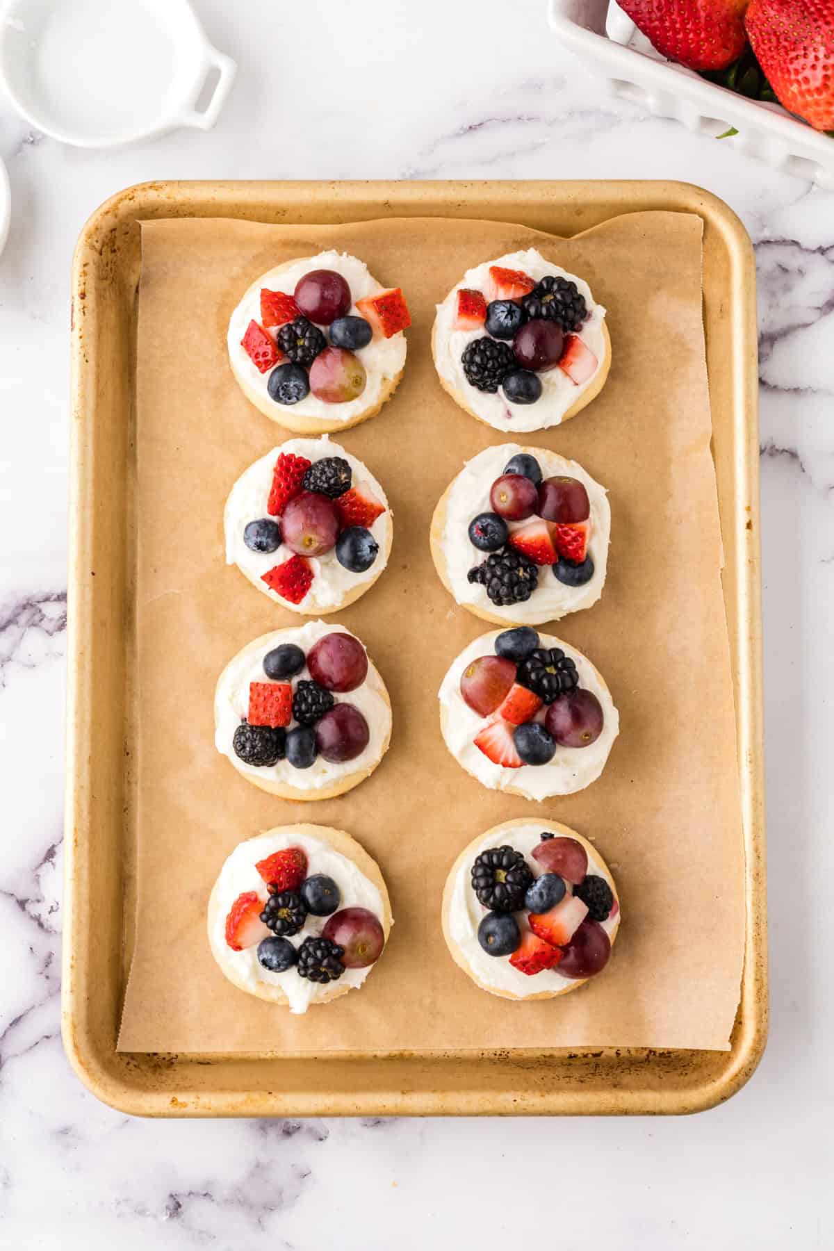 fruit pizza cookies on parchment on a half sheet pan.