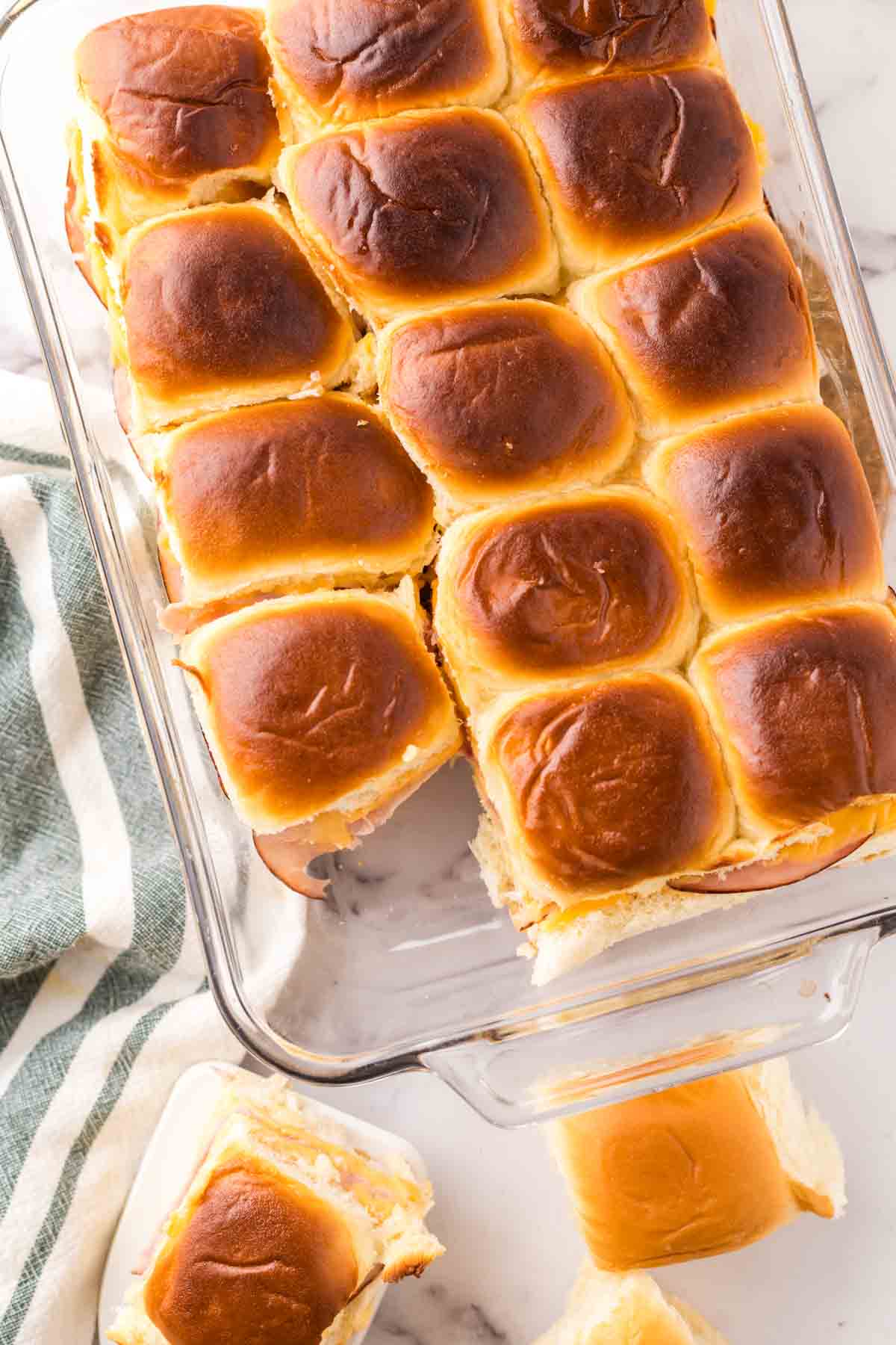 casserole dish with baked ham and cheese sliders on hawaiian rolls.