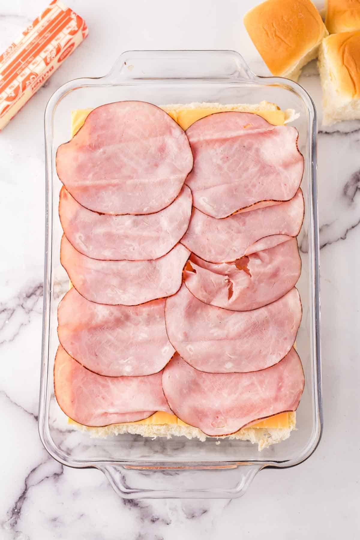 half hawaiian rolls with cheese and ham on top in a baking dish.