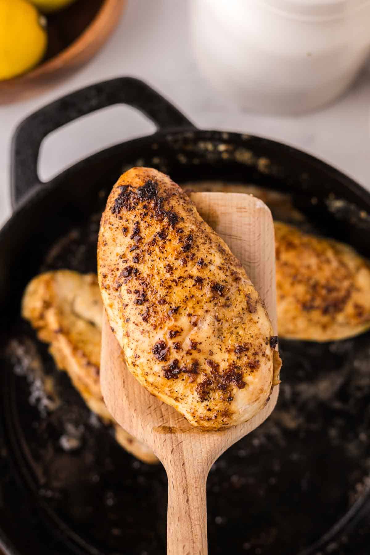 wooden spatula over a cast iron skillet with the Lemon Pepper Chicken Recipe.