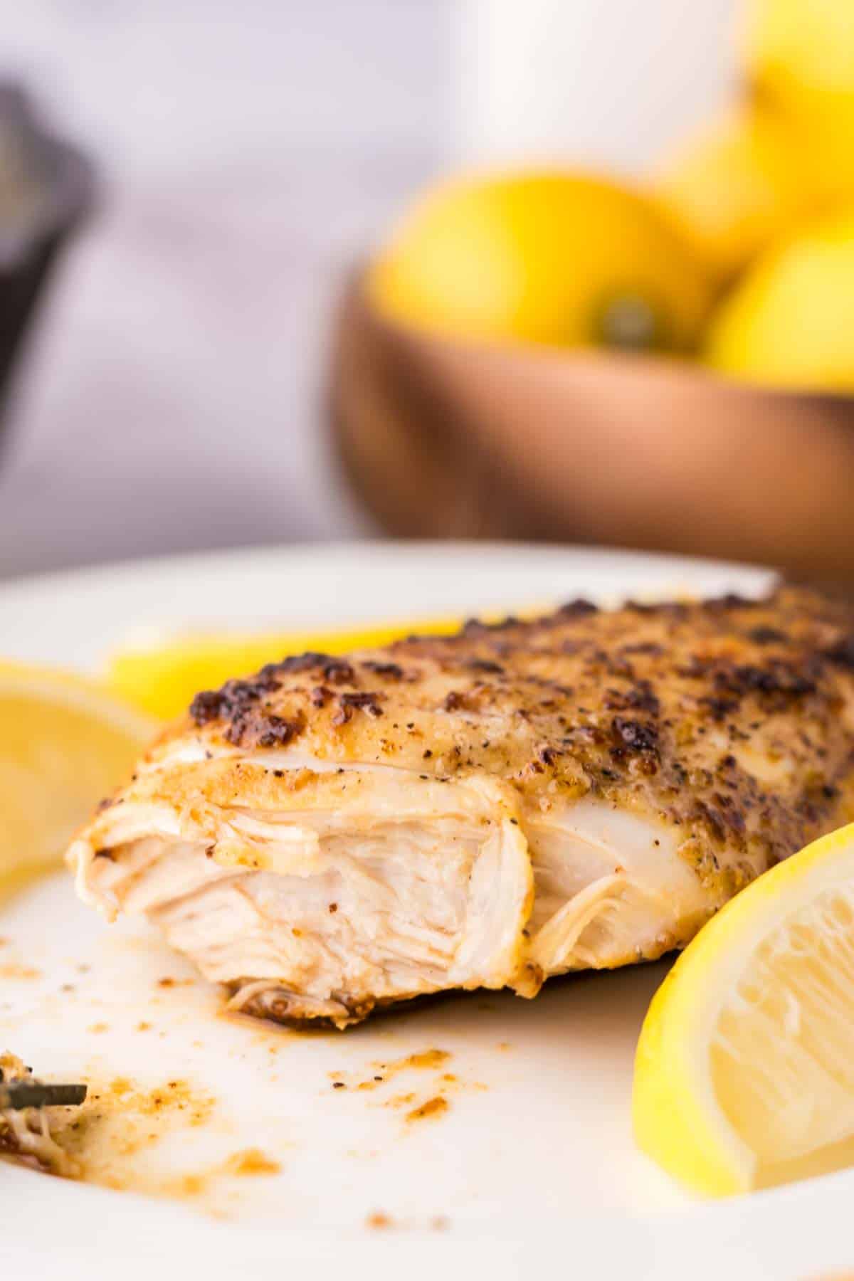 white plate with lemon pepper chicken breast surrounded by fresh lemons with a bite out of it.