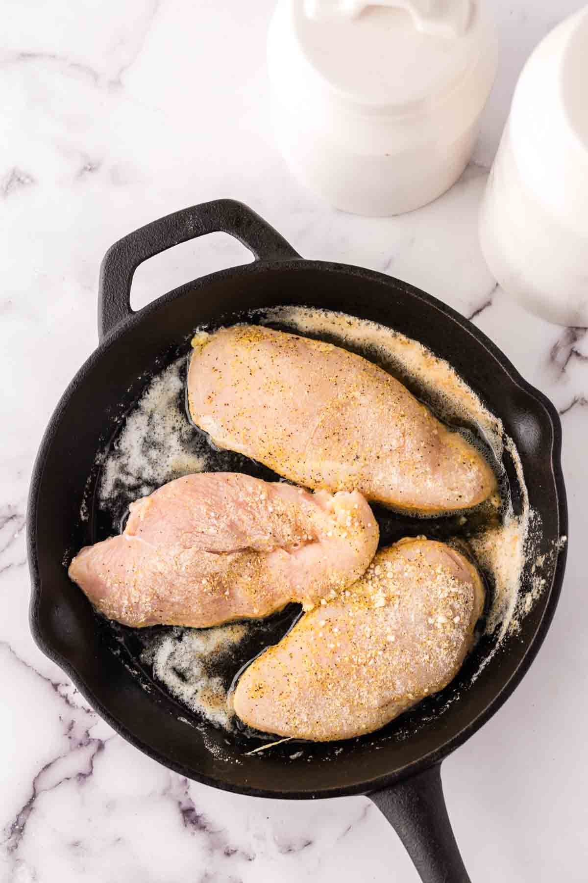 breaded raw chicken breast going into a cast iron pan, ready to make lemon pepper chicken.