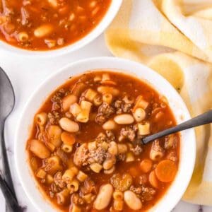 small white bowl with pasta fagioli soup recipe with a black spoon in it ready to eat.