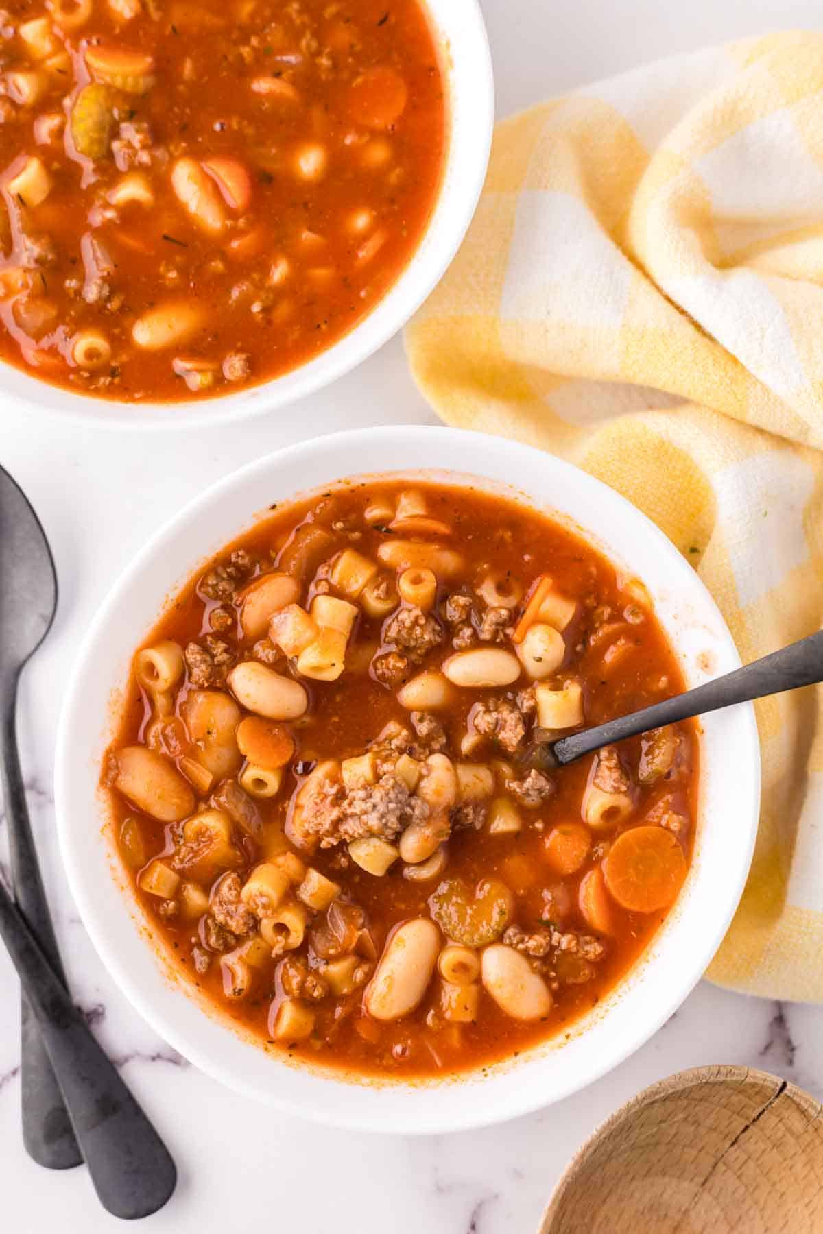 small white bowl with pasta fagioli soup recipe with a black spoon in it ready to eat.