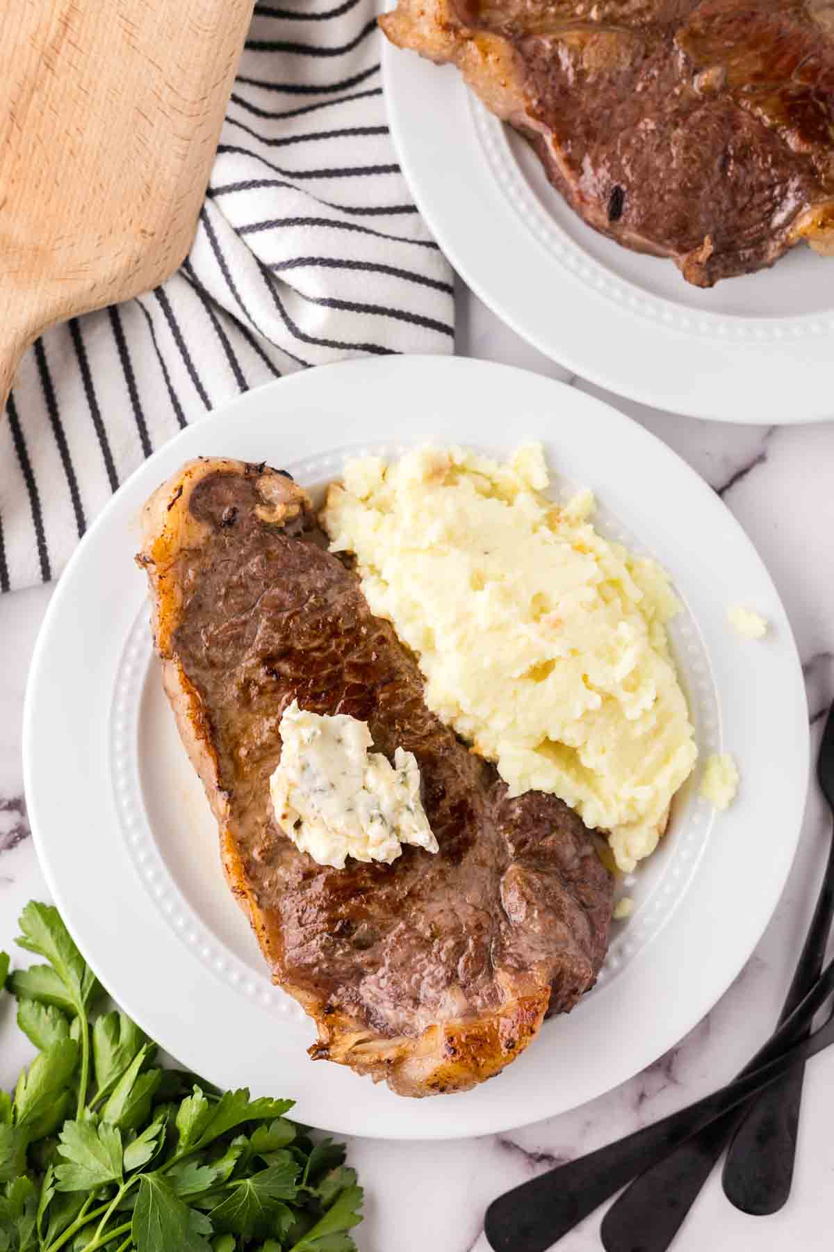 a steak dinner on a white plate with mashed potatoes on the side with compound butter on top.