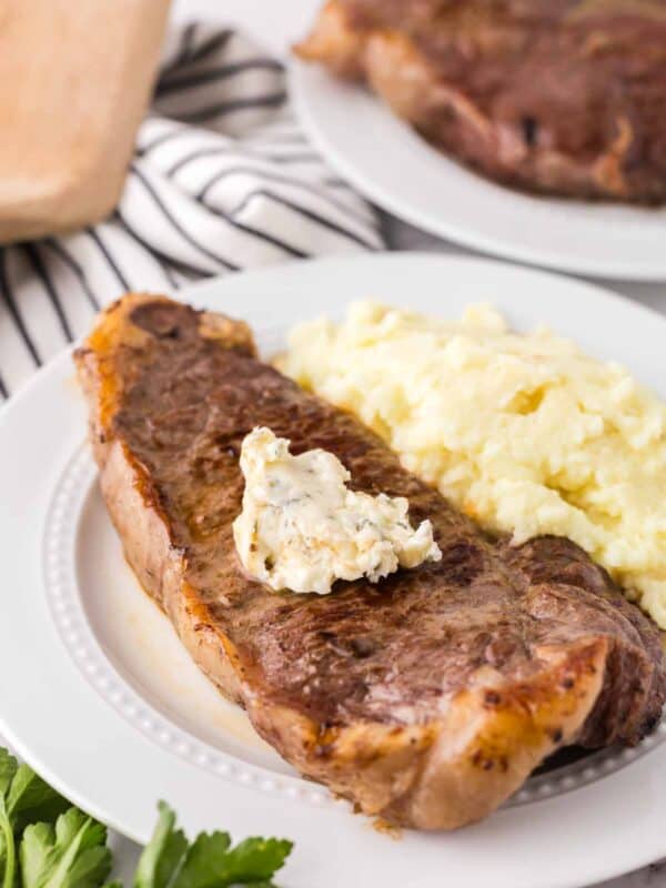 a steak dinner on a white plate with mashed potatoes on the side with compound butter on top.