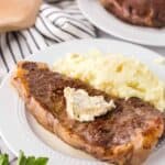 a steak dinner on a white plate with mashed potatoes on the side with compound butter on top.