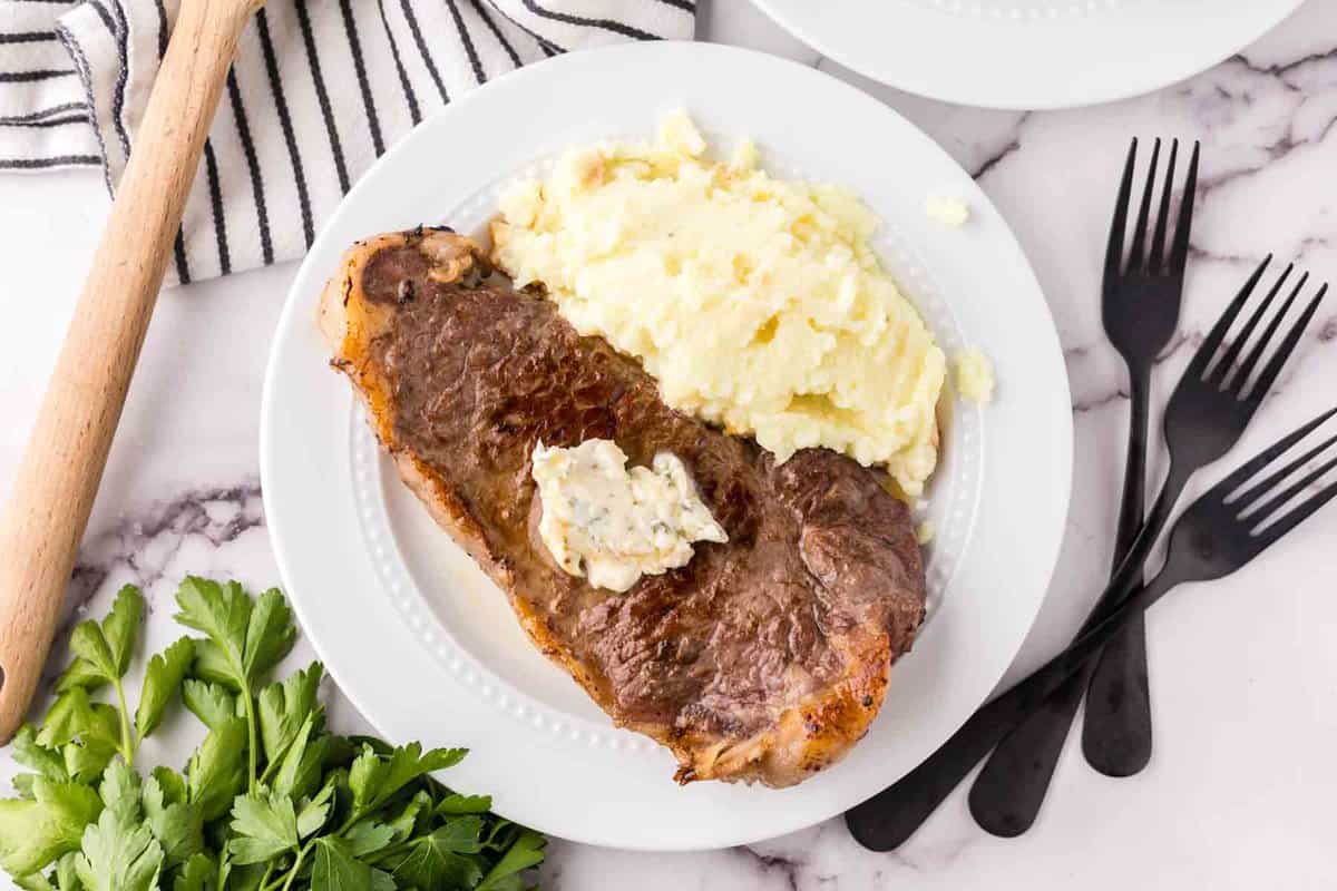 a steak dinner on a white plate with mashed potatoes on the side with compound butter on top.