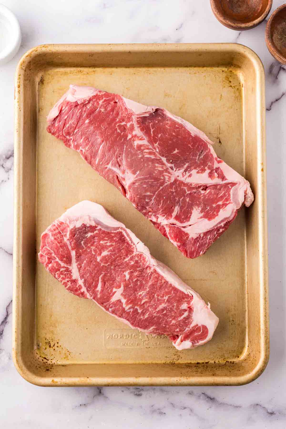 two raw steaks on a sheet pan.